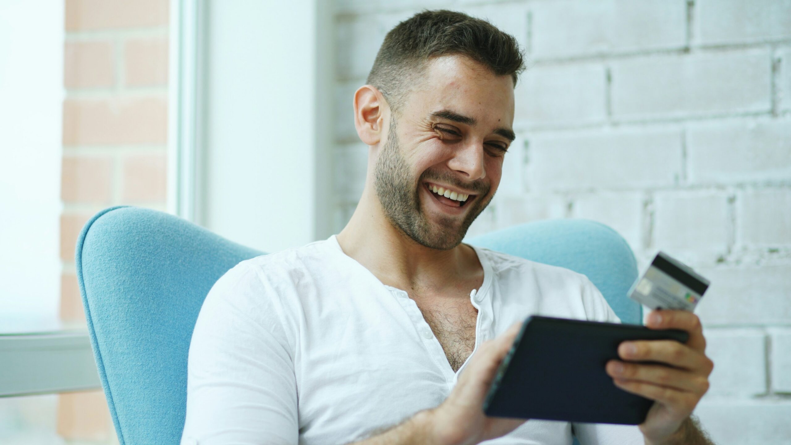 Tabletet és bankkártyát tartó, elégedetten mosolygó férfi, aki épp egy sikeres online pénzváltási tranzakciót vagy digitális utalást hajt végre.